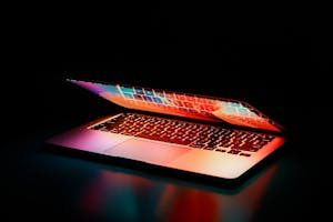 Laptop partially opened, emitting vibrant multicolored lights in dark setting.